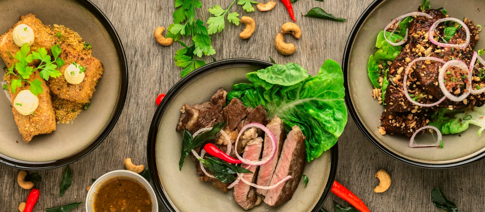 An overhead spread of three plated weeknight dinners on a wooden table